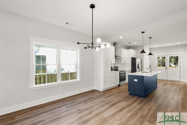 kitchen featuring appliances with stainless steel finishes, light wood-type flooring, pendant lighting, a center island with sink, and white cabinets