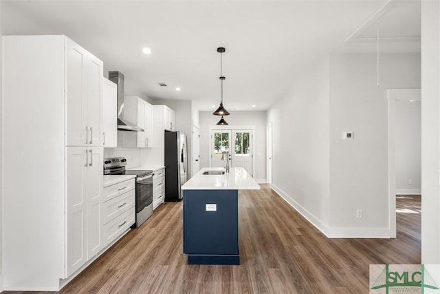 kitchen with a kitchen island with sink, wall chimney exhaust hood, appliances with stainless steel finishes, decorative light fixtures, and white cabinetry