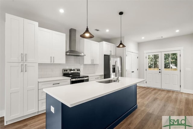 kitchen featuring wall chimney range hood, decorative light fixtures, light hardwood / wood-style floors, white cabinetry, and stainless steel appliances