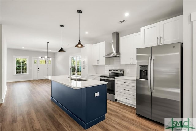 kitchen with appliances with stainless steel finishes, wall chimney exhaust hood, sink, a center island with sink, and white cabinetry