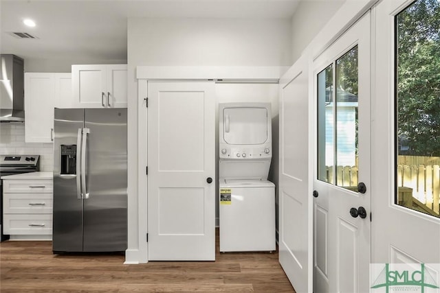 clothes washing area with hardwood / wood-style floors and stacked washing maching and dryer