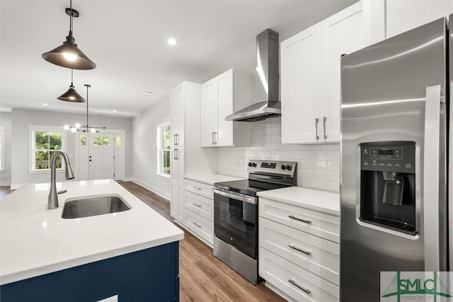 kitchen featuring wall chimney exhaust hood, stainless steel appliances, sink, wood-type flooring, and decorative light fixtures