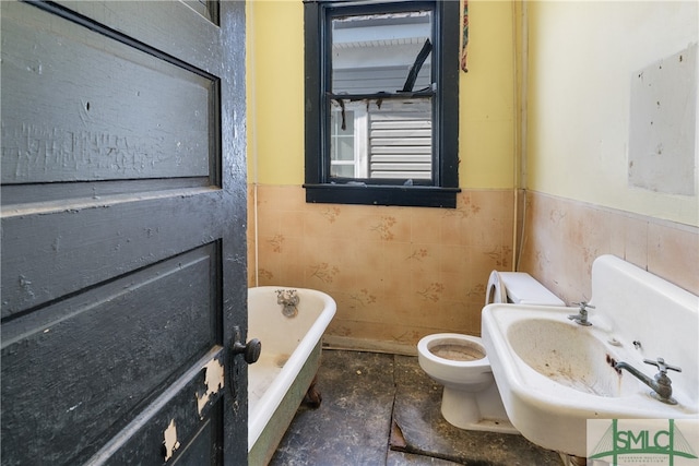 bathroom with sink, a tub to relax in, toilet, and tile walls