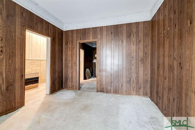 empty room with a fireplace, wooden walls, carpet floors, and ornamental molding