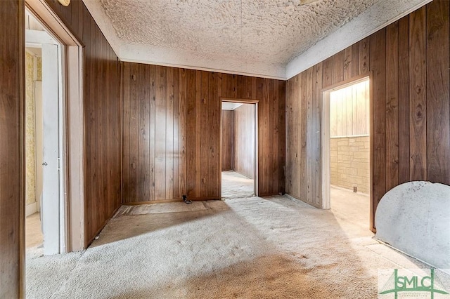 carpeted spare room featuring wood walls and a textured ceiling