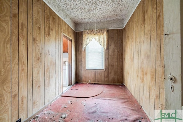 carpeted empty room with wooden walls and a textured ceiling