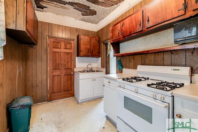 kitchen with gas range gas stove, sink, white cabinets, and wooden walls