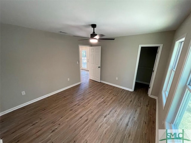 unfurnished bedroom with dark hardwood / wood-style floors, ceiling fan, a spacious closet, and multiple windows