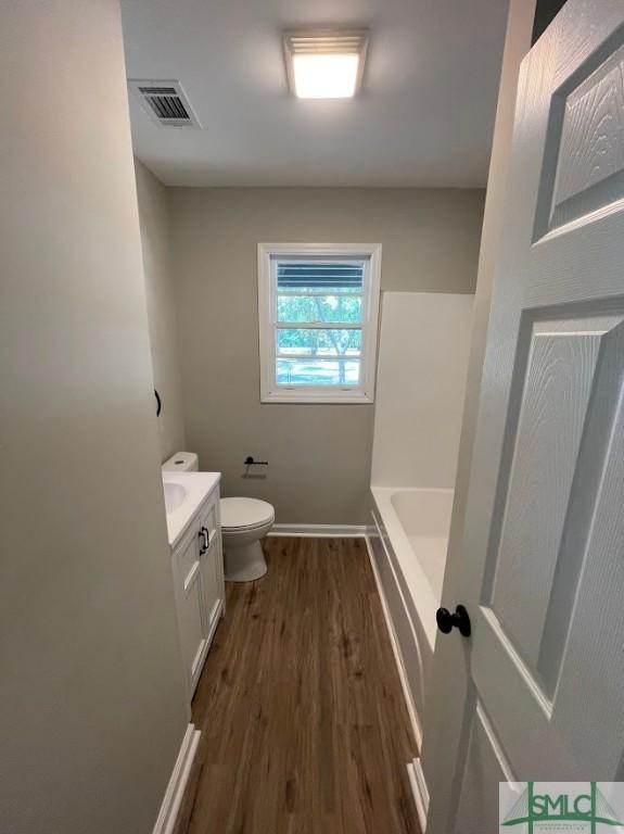 bathroom with a washtub, toilet, vanity, and hardwood / wood-style flooring