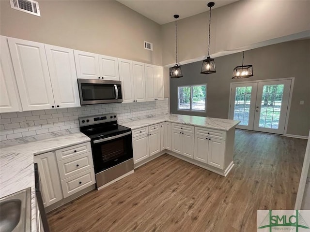 kitchen with white cabinetry, a high ceiling, kitchen peninsula, appliances with stainless steel finishes, and hardwood / wood-style flooring