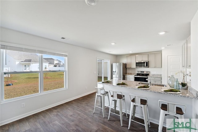 kitchen featuring light stone countertops, sink, stainless steel appliances, dark hardwood / wood-style flooring, and a kitchen bar