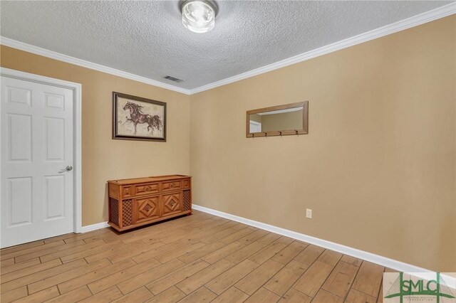 empty room with a textured ceiling, light wood-type flooring, and crown molding