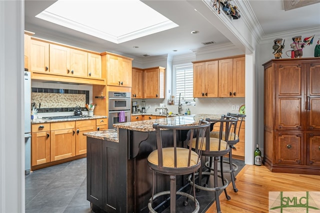 kitchen featuring light stone countertops, stainless steel double oven, dark hardwood / wood-style flooring, a kitchen bar, and ornamental molding