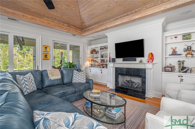 living room with a tile fireplace, ceiling fan, built in features, hardwood / wood-style floors, and ornamental molding