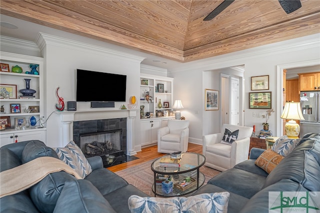 living room featuring a tile fireplace, ceiling fan, built in features, light wood-type flooring, and ornamental molding