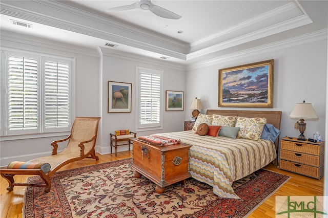 bedroom featuring a raised ceiling, light hardwood / wood-style flooring, ceiling fan, and crown molding