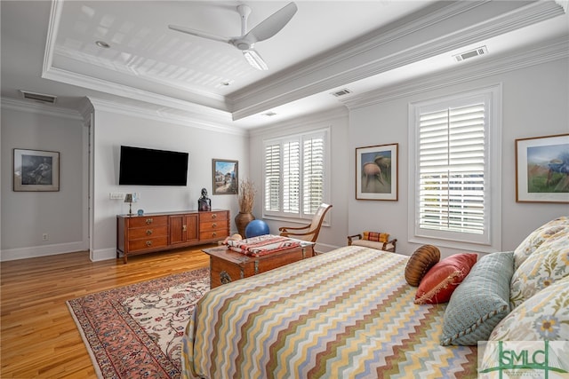 bedroom with ceiling fan, light hardwood / wood-style floors, ornamental molding, and a tray ceiling