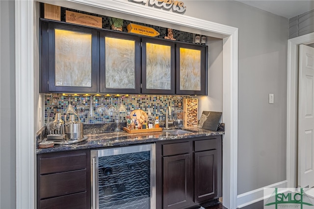 bar featuring dark brown cabinetry, sink, wine cooler, dark stone counters, and decorative backsplash