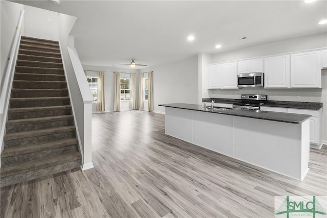 kitchen featuring appliances with stainless steel finishes, ceiling fan, a kitchen island with sink, white cabinets, and light hardwood / wood-style floors