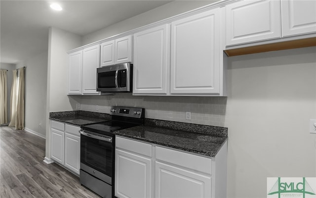 kitchen featuring white cabinets, dark stone counters, appliances with stainless steel finishes, and light hardwood / wood-style flooring