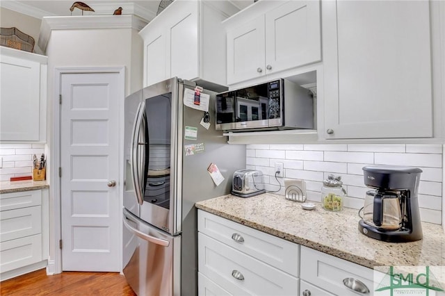 kitchen with appliances with stainless steel finishes, tasteful backsplash, white cabinetry, and light hardwood / wood-style flooring