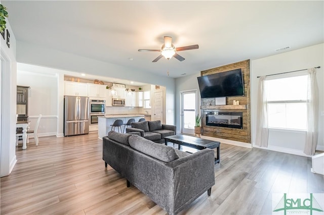 living room with ceiling fan, a fireplace, and light wood-type flooring