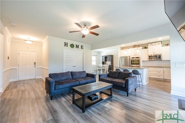 living room featuring ceiling fan, light hardwood / wood-style floors, and crown molding