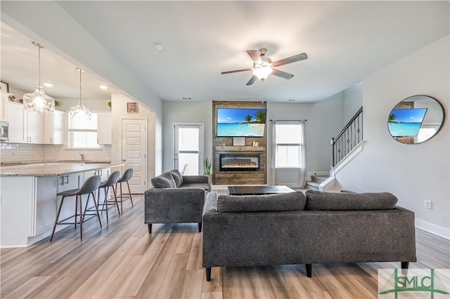 living room with ceiling fan, a large fireplace, and light wood-type flooring