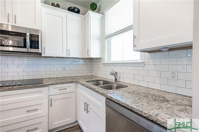 kitchen with white cabinetry, sink, stainless steel appliances, light stone counters, and decorative backsplash