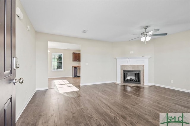 unfurnished living room with a tile fireplace, ceiling fan, and dark hardwood / wood-style flooring