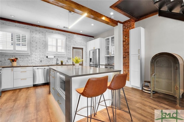 kitchen with a center island, light wood-type flooring, appliances with stainless steel finishes, brick wall, and white cabinets