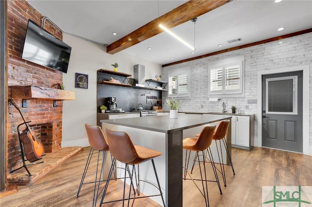 kitchen featuring a kitchen island, a breakfast bar, beamed ceiling, white cabinetry, and light hardwood / wood-style flooring