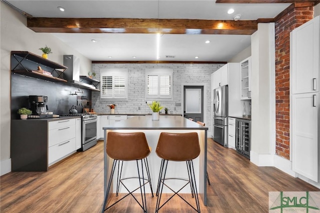 kitchen with brick wall, a kitchen island, beamed ceiling, white cabinets, and stainless steel appliances