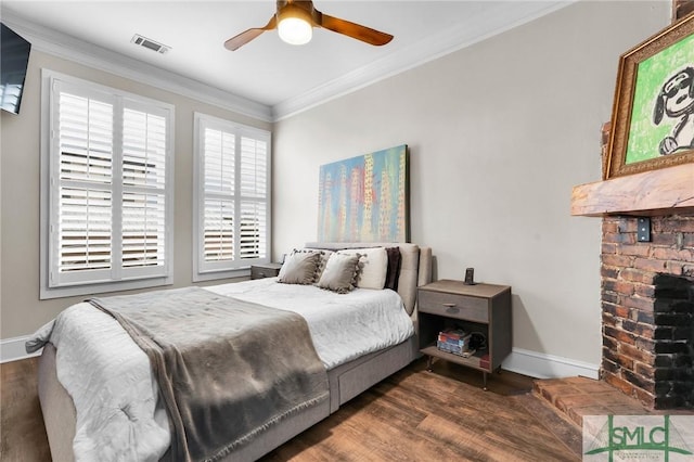 bedroom with a brick fireplace, crown molding, dark wood-type flooring, and ceiling fan