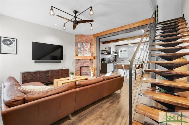 living room with beam ceiling, wood-type flooring, a brick fireplace, and ceiling fan