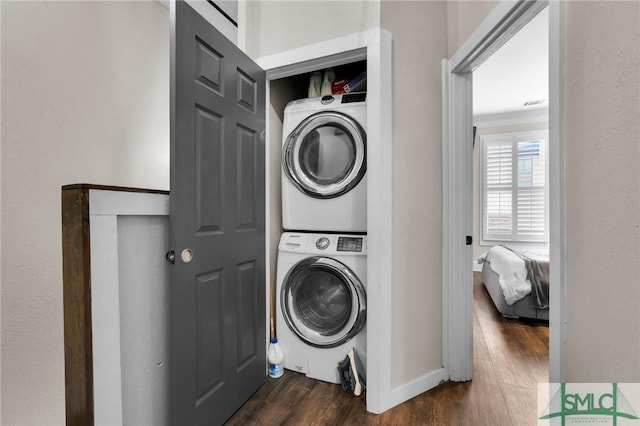 laundry area with stacked washing maching and dryer and dark hardwood / wood-style flooring