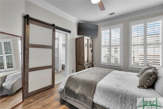 bedroom with crown molding, ensuite bath, ceiling fan, wood-type flooring, and a barn door