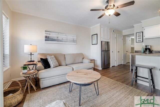 living area with a ceiling fan, baseboards, dark wood finished floors, and ornamental molding