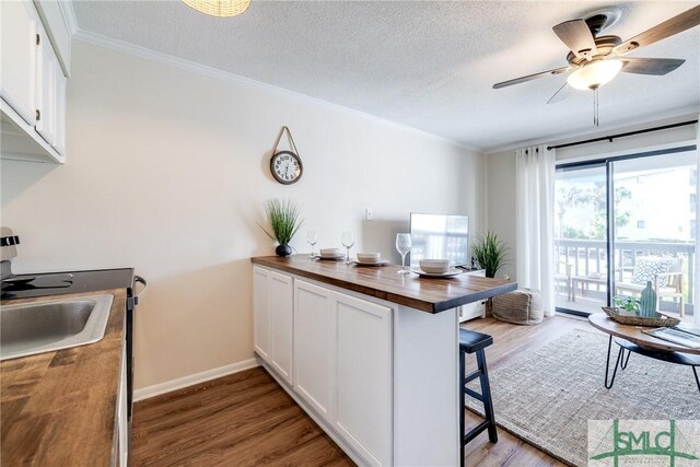 kitchen with a breakfast bar area, wooden counters, wood finished floors, a peninsula, and ornamental molding