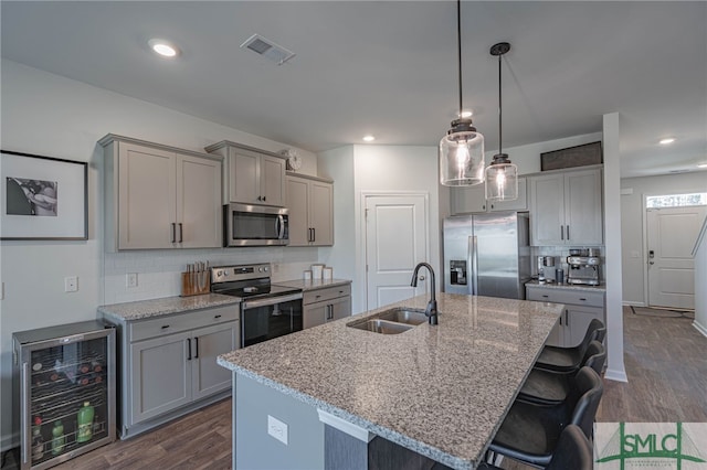 kitchen featuring light stone countertops, appliances with stainless steel finishes, beverage cooler, sink, and a center island with sink