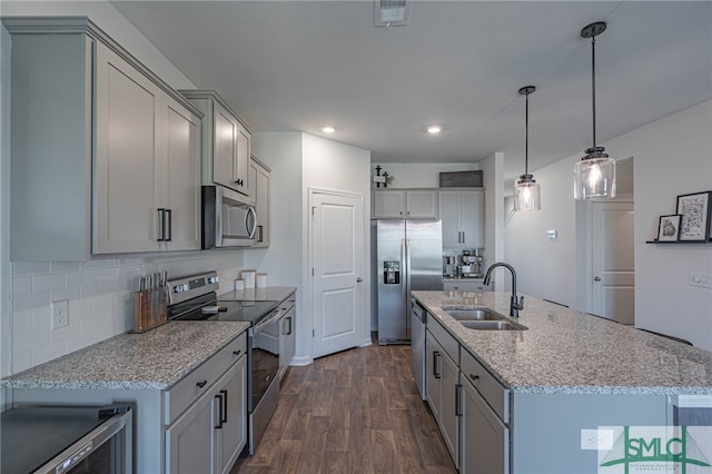 kitchen with stainless steel appliances, a kitchen island with sink, sink, decorative light fixtures, and dark hardwood / wood-style floors