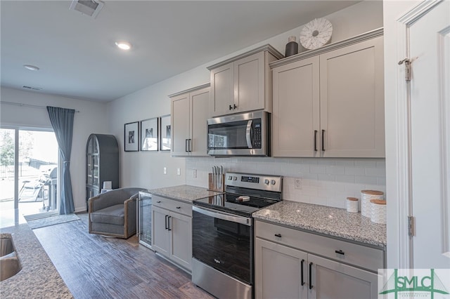 kitchen featuring appliances with stainless steel finishes, dark hardwood / wood-style flooring, backsplash, light stone counters, and gray cabinets