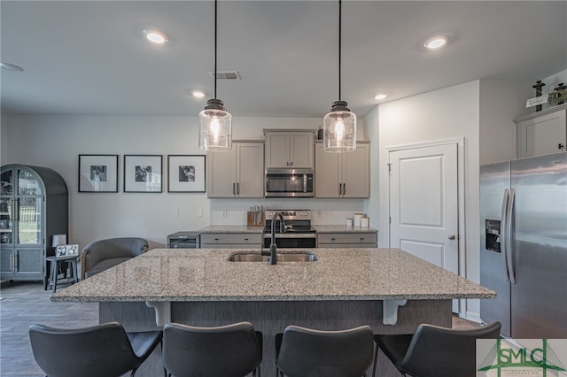 kitchen with decorative light fixtures, light stone counters, stainless steel appliances, and an island with sink