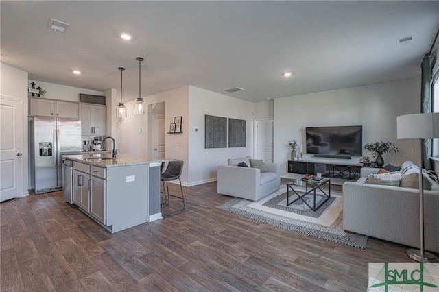 kitchen featuring light stone counters, an island with sink, pendant lighting, gray cabinets, and appliances with stainless steel finishes