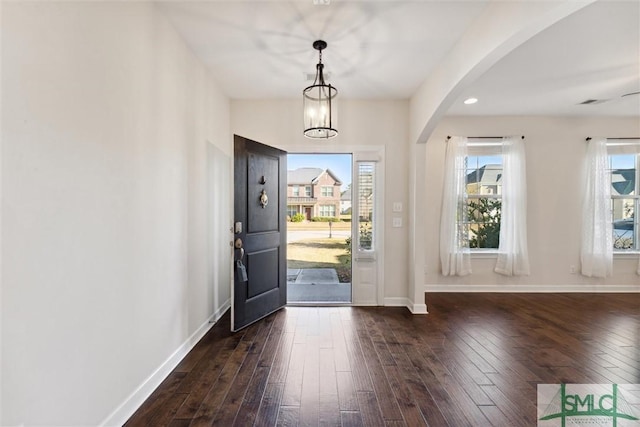 foyer with hardwood / wood-style flooring, baseboards, arched walkways, and a notable chandelier