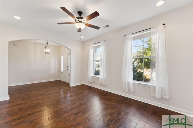 empty room featuring arched walkways, hardwood / wood-style flooring, recessed lighting, visible vents, and baseboards