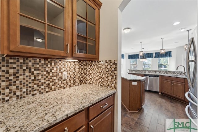 kitchen with brown cabinetry, decorative backsplash, appliances with stainless steel finishes, light stone counters, and a sink