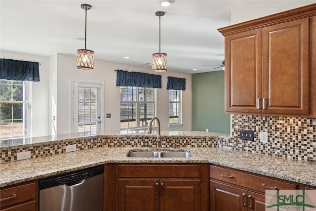 kitchen with light stone counters, decorative light fixtures, backsplash, stainless steel dishwasher, and a sink