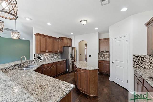 kitchen with arched walkways, decorative backsplash, a sink, and stainless steel fridge with ice dispenser