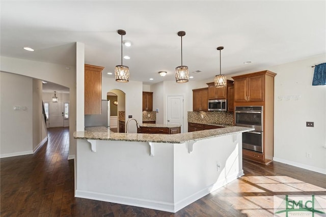 kitchen with stainless steel appliances, arched walkways, brown cabinets, and a kitchen bar